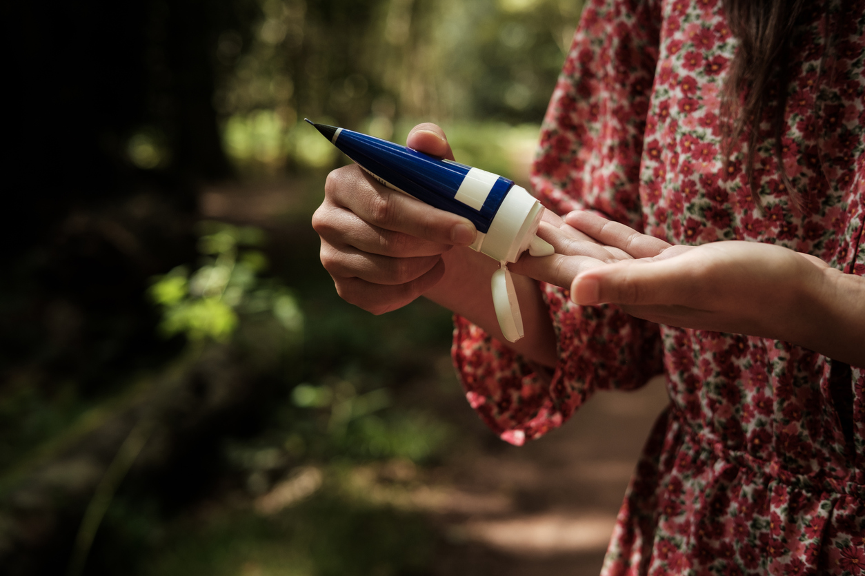 Woman wearing a floral dress is squeezing moisturizing cream from a tube onto her hands while standing in a forest
