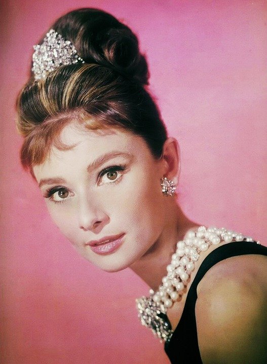 Audrey Hepburn wearing a black dress, chunky pearl necklace, tiara and sparkly earrings