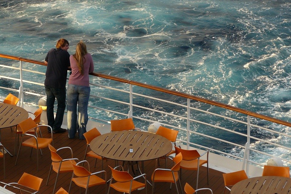 A couple standing by the cruise ship rails, observing the water