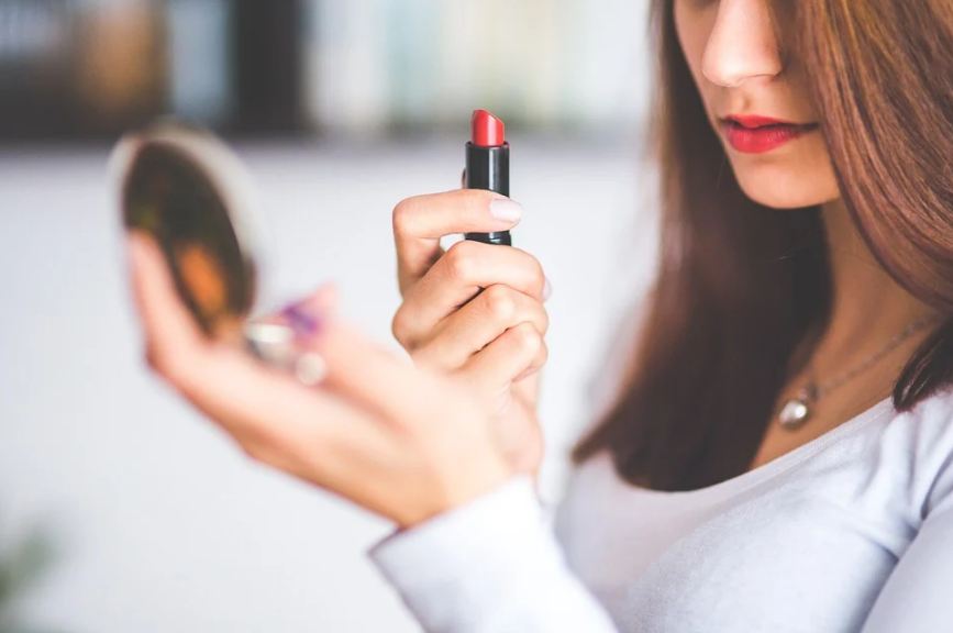 woman applying lipstick and using a compact mirror