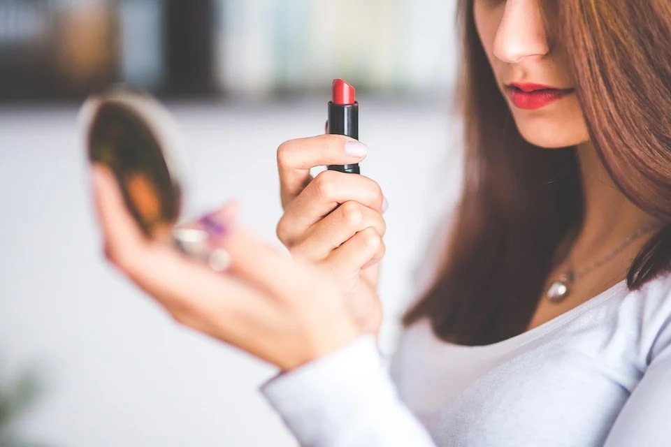 A woman applying lipstick looking into a mirror