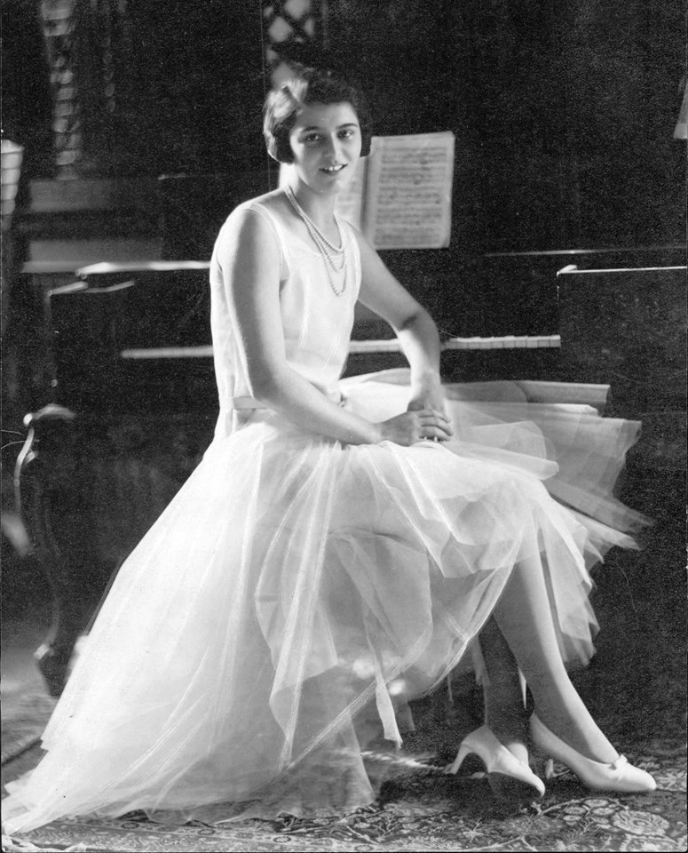 a woman sitting by the piano wearing a robe de style dress from 1929