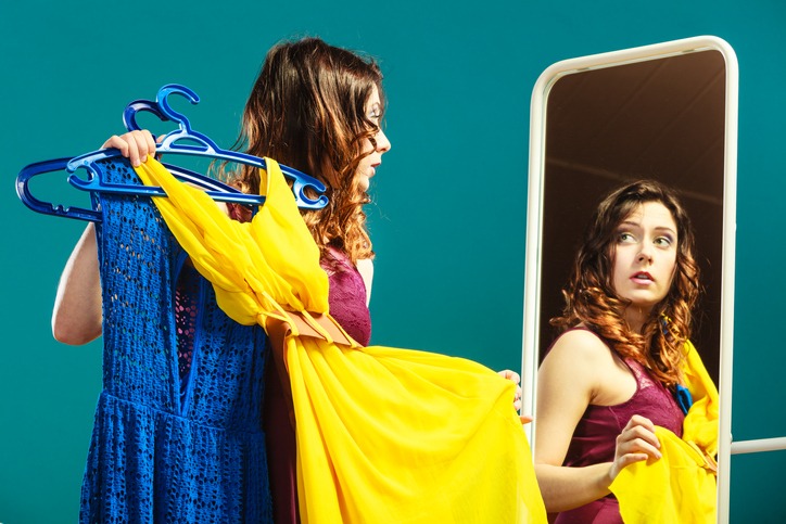 woman shopper holds hangers with clothes looking in mirror