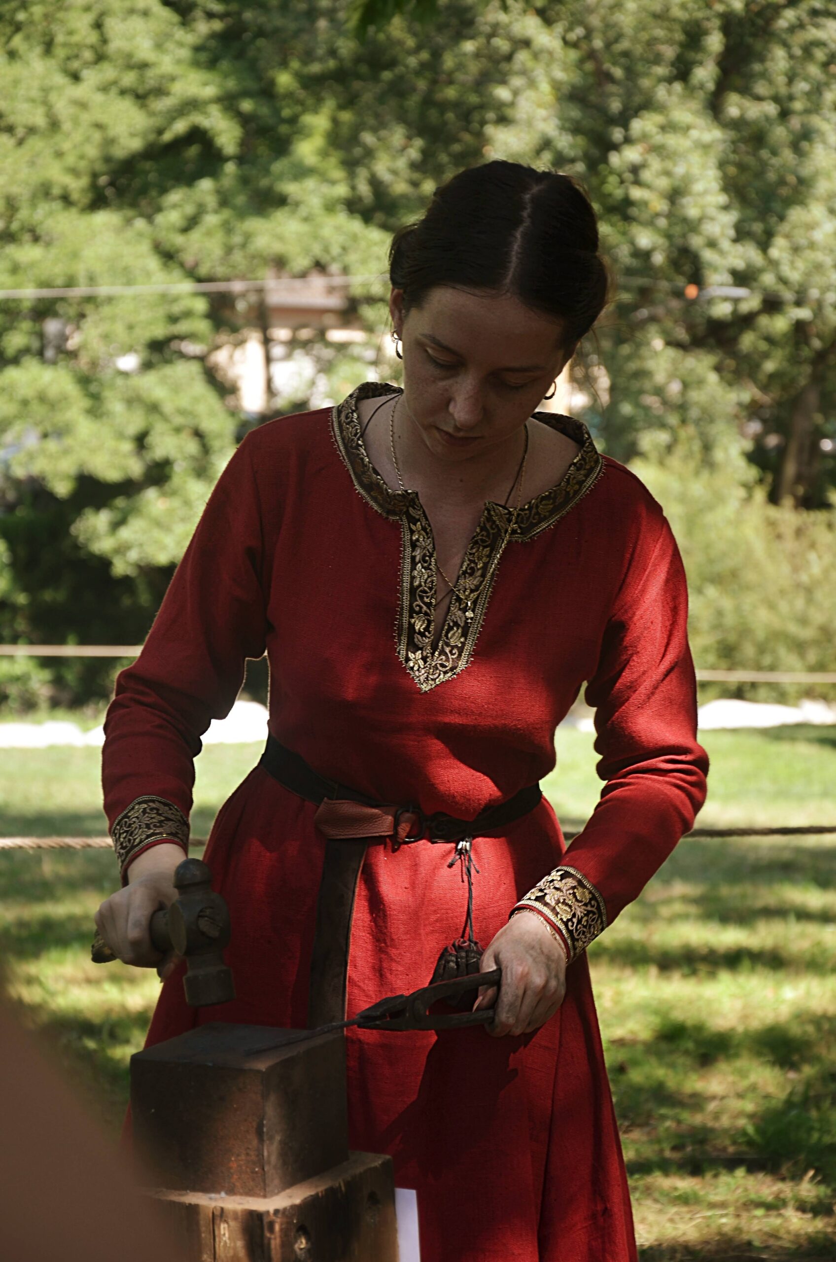 A woman in red medieval clothing holding a hammer and pliers